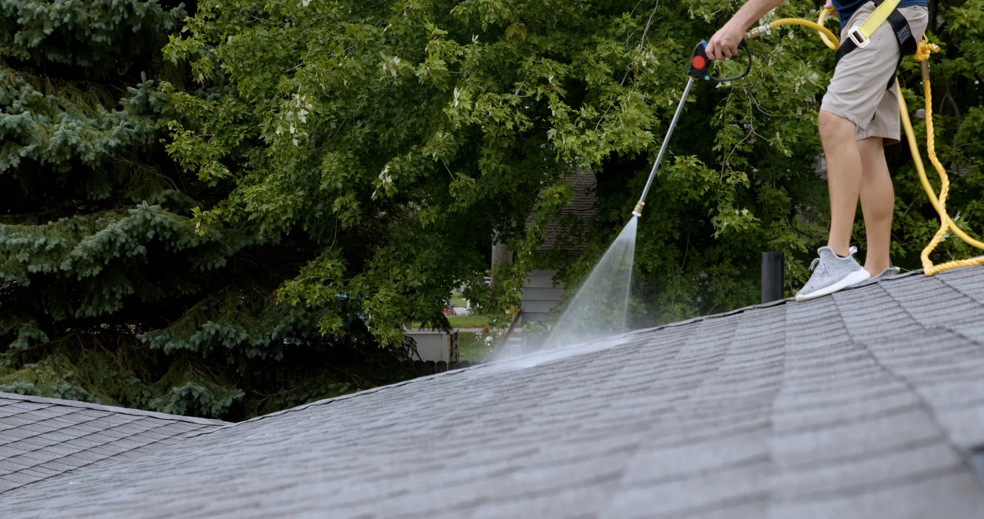 A certified applicator spraying ShingleLock across an asphalt shingle roof